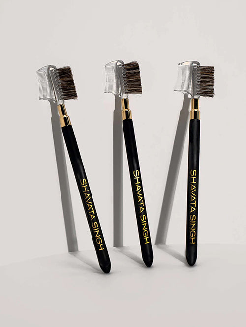 Three eyebrow brushes with black handles and gold accents, displayed side by side with the comb sides facing forward.
